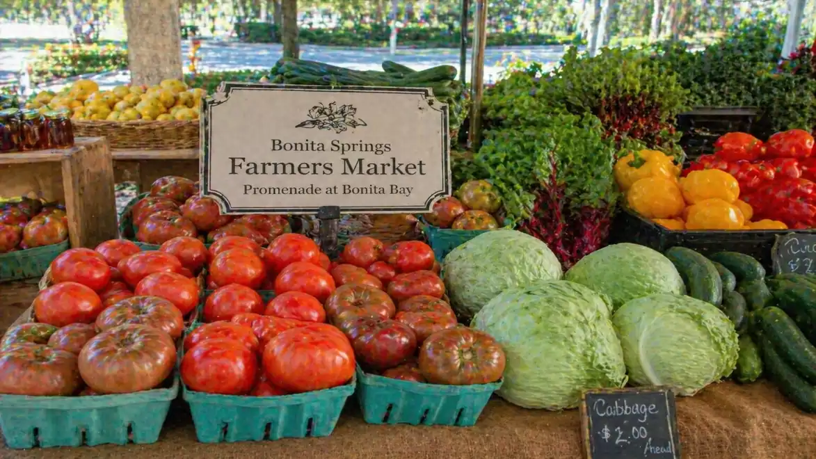 Fresh fruit and vegetable stall at Bonita Springs Farmers Market featuring tomatoes, bell peppers, and cabbage.