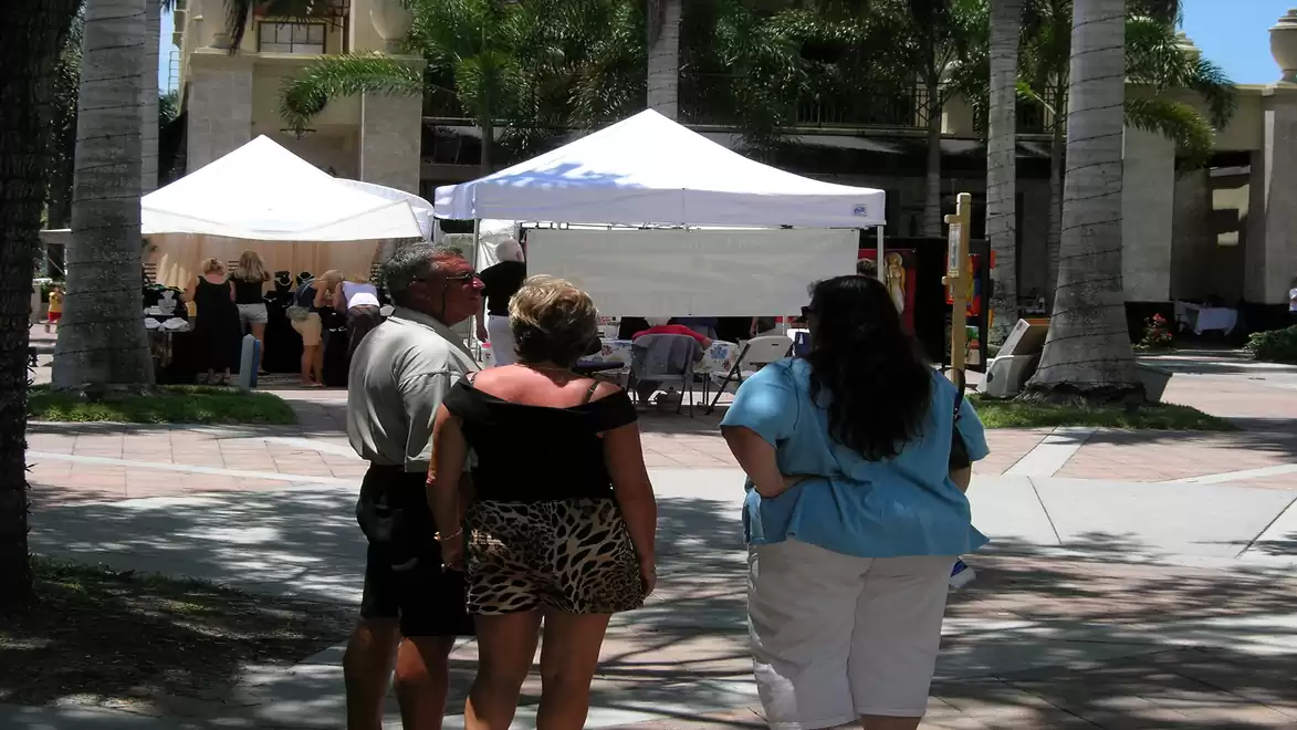 Three people on a sunlit square with white market booths in the background.