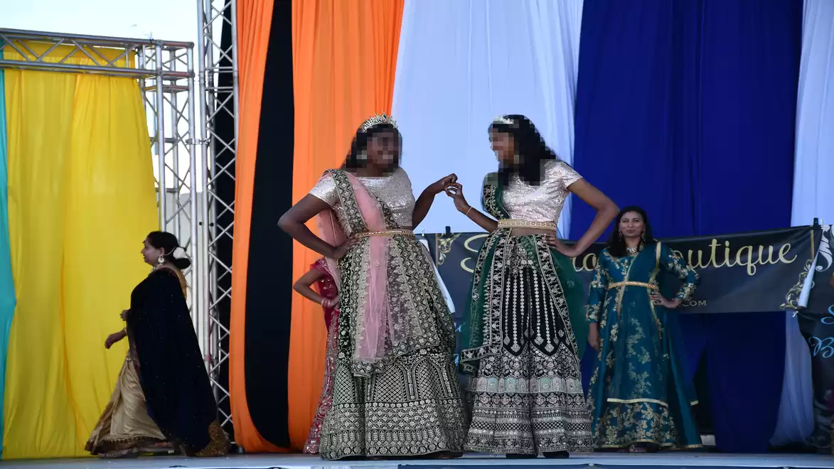 Fashion show with two women in traditional dresses on a stage with colorful curtains in the background.