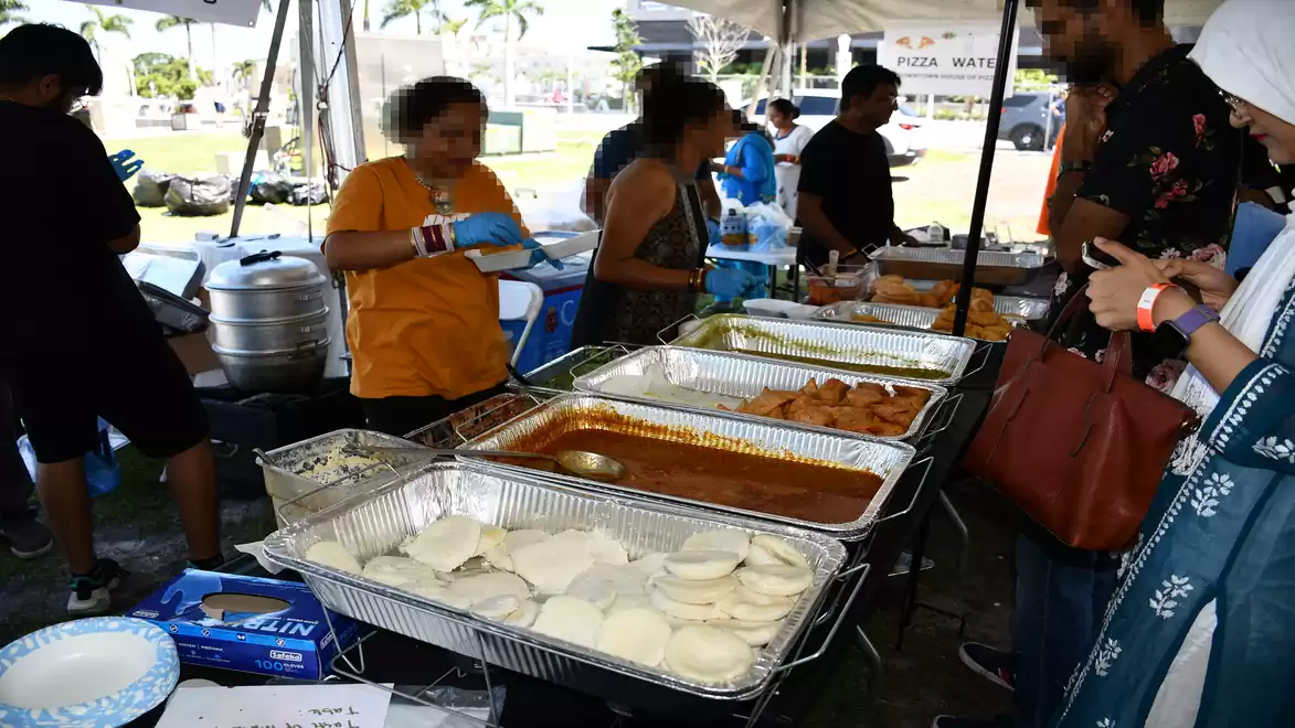 People serving themselves at a buffet with various dishes at an outdoor event.