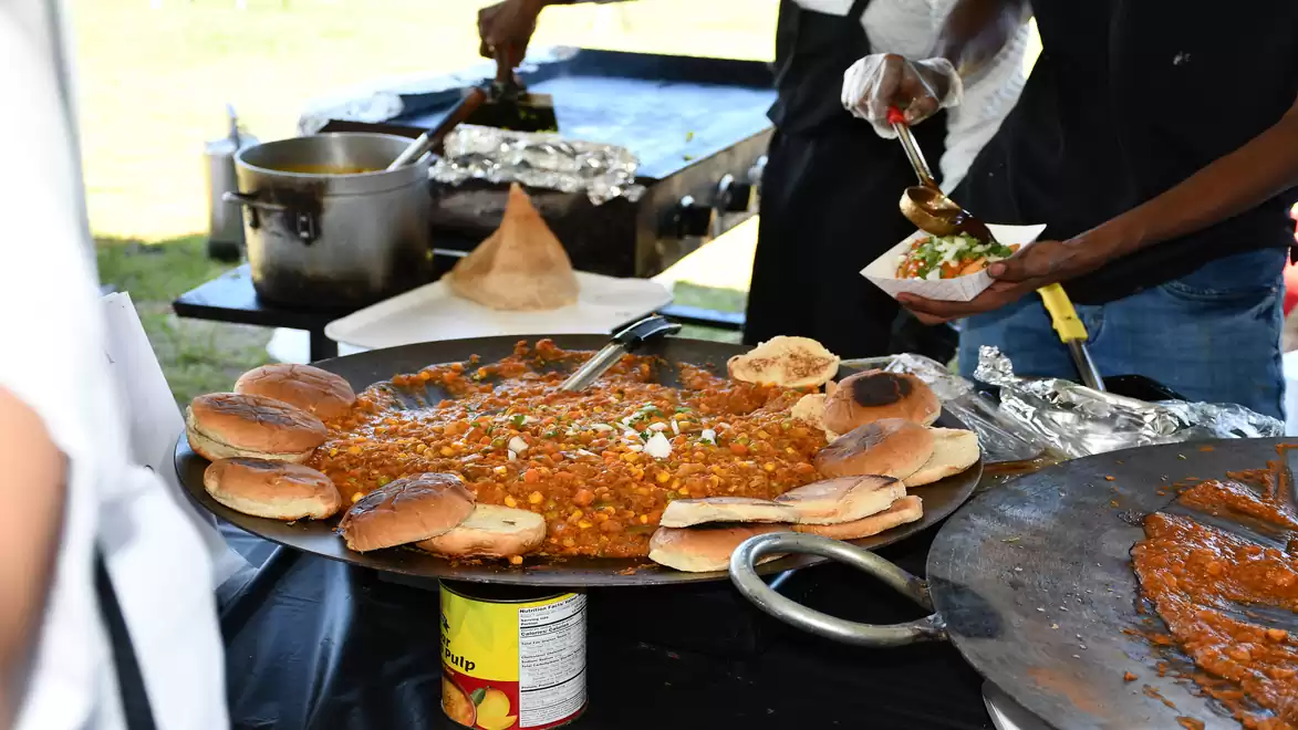 Large pan with curry dish and buns on a table at a street market.