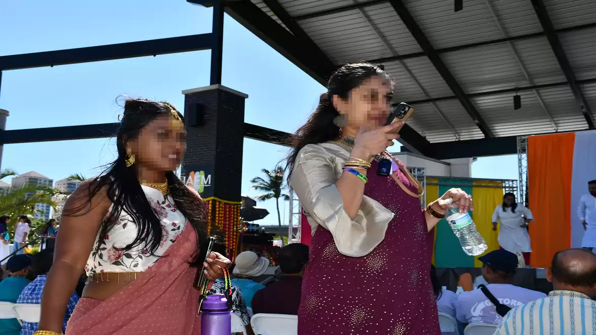 Two women in traditional clothing stand in front of an audience at an outdoor event.
