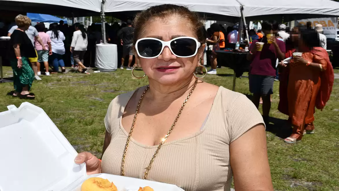 Woman wearing sunglasses holds food at an outdoor event.