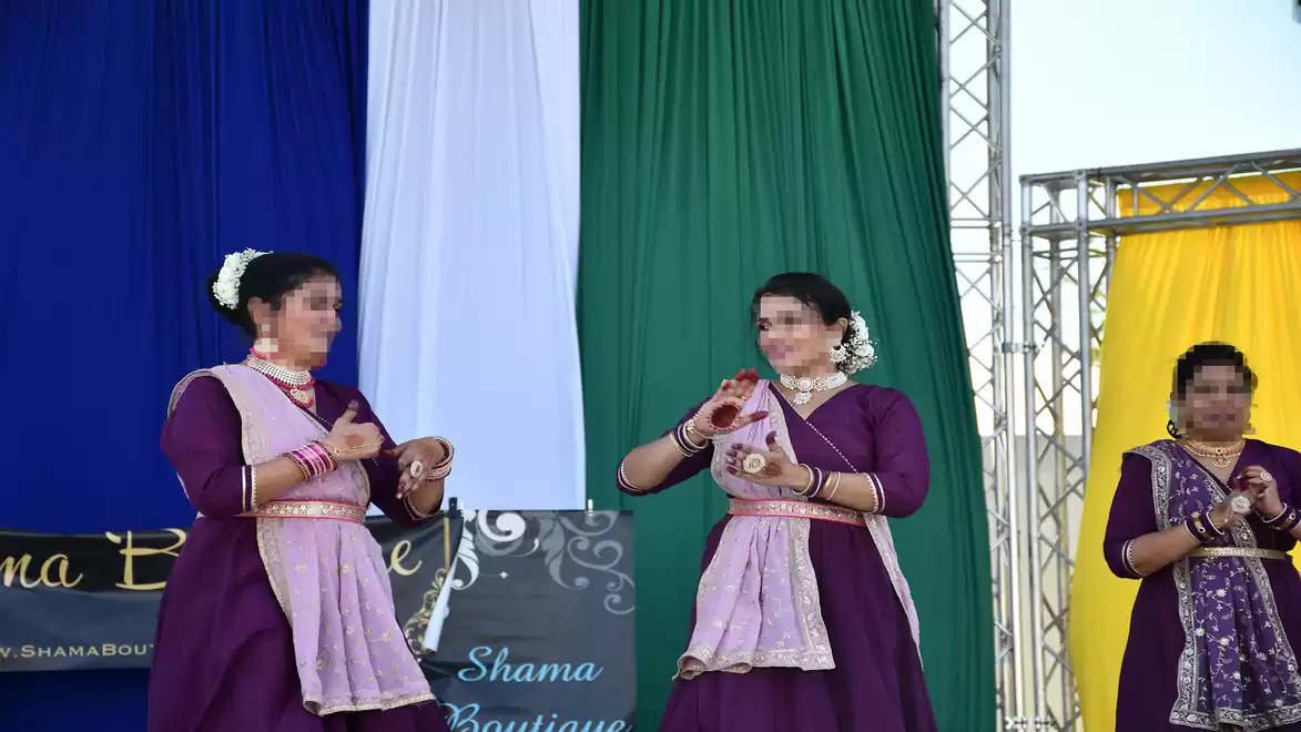 Three women in traditional purple dresses performing a cultural dance on stage.