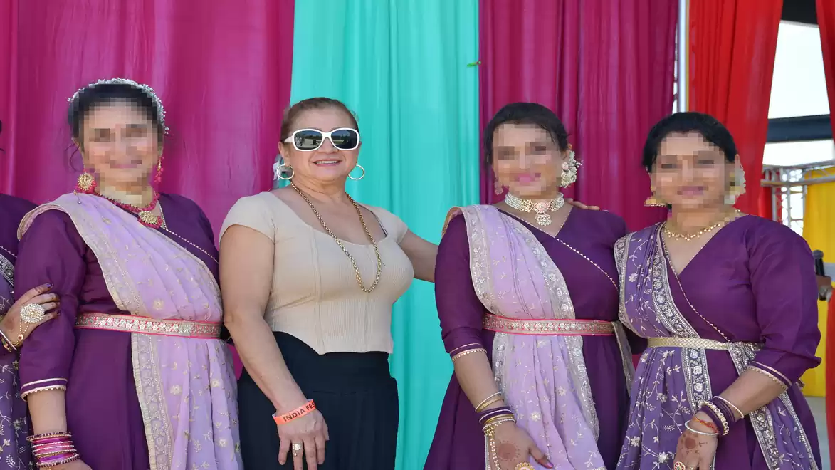 Five women in traditional Indian dresses posing in front of a colorful backdrop.