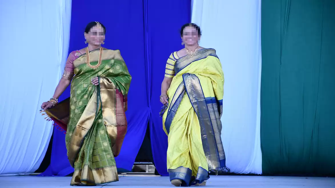 Two women in traditional saris on a runway, surrounded by colorful hanging fabrics.