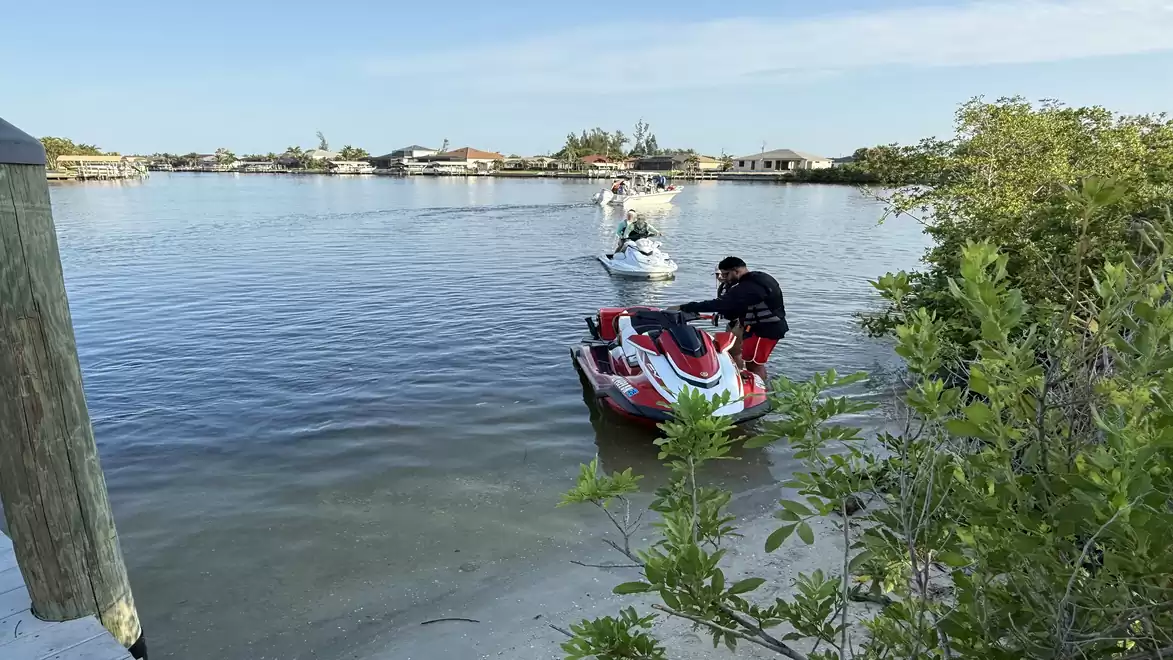 A man on a jet ski on a sunny day on a calm lake with another jet ski in the background.