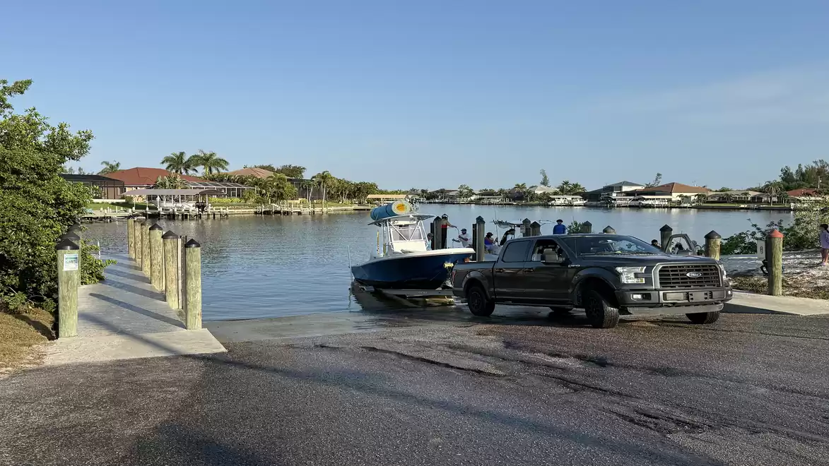 A black pickup truck pulls a boat out of the water on a ramp, surrounded by water and green landscape.