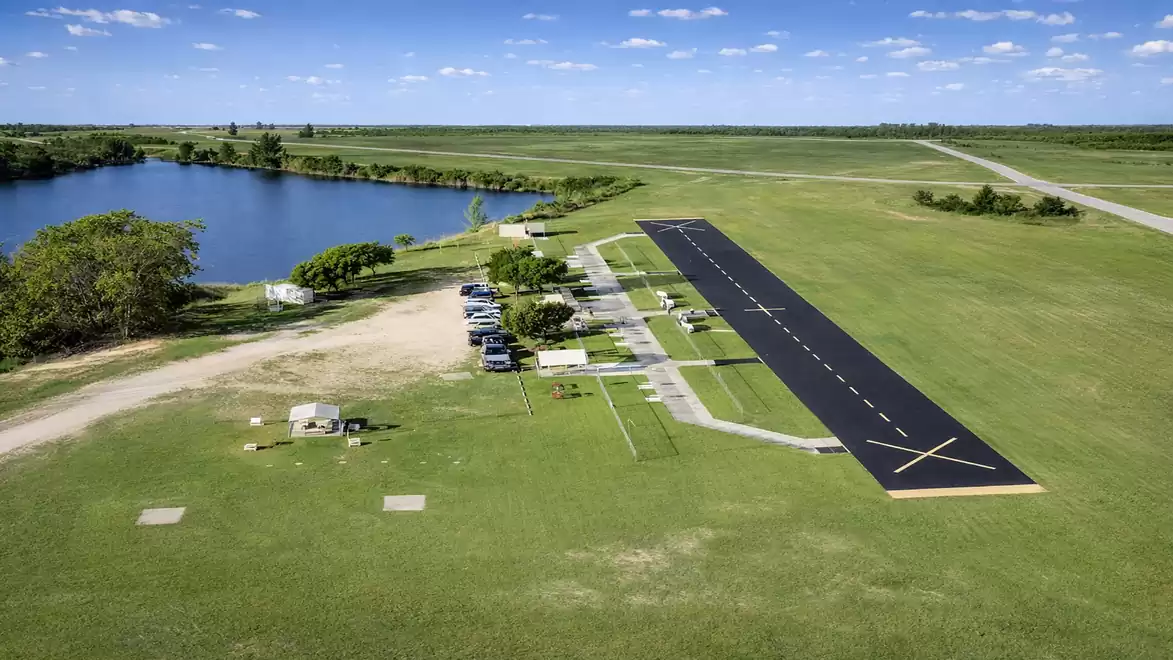 Aerial view of a small airstrip with a runway and an adjacent lake, surrounded by green fields.