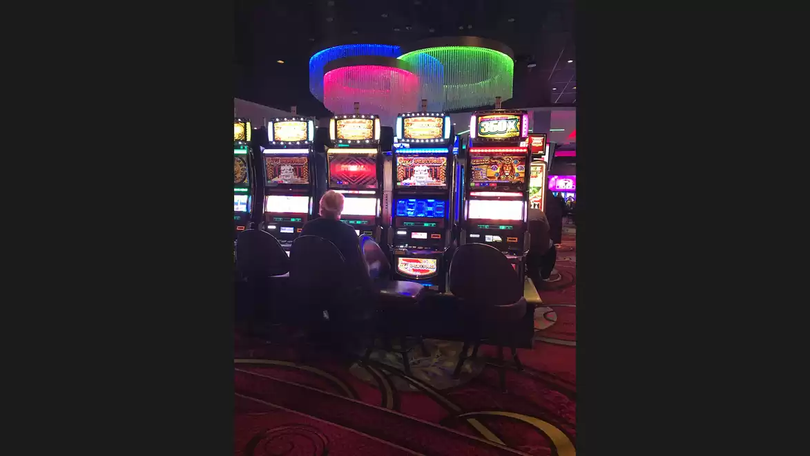 Slot machines in a casino with colorful lights and people playing.