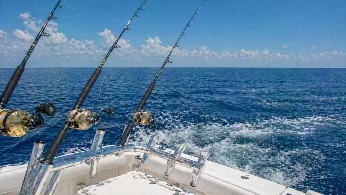 Sport fishing on the open sea with multiple fishing rods and a bright blue sky.
