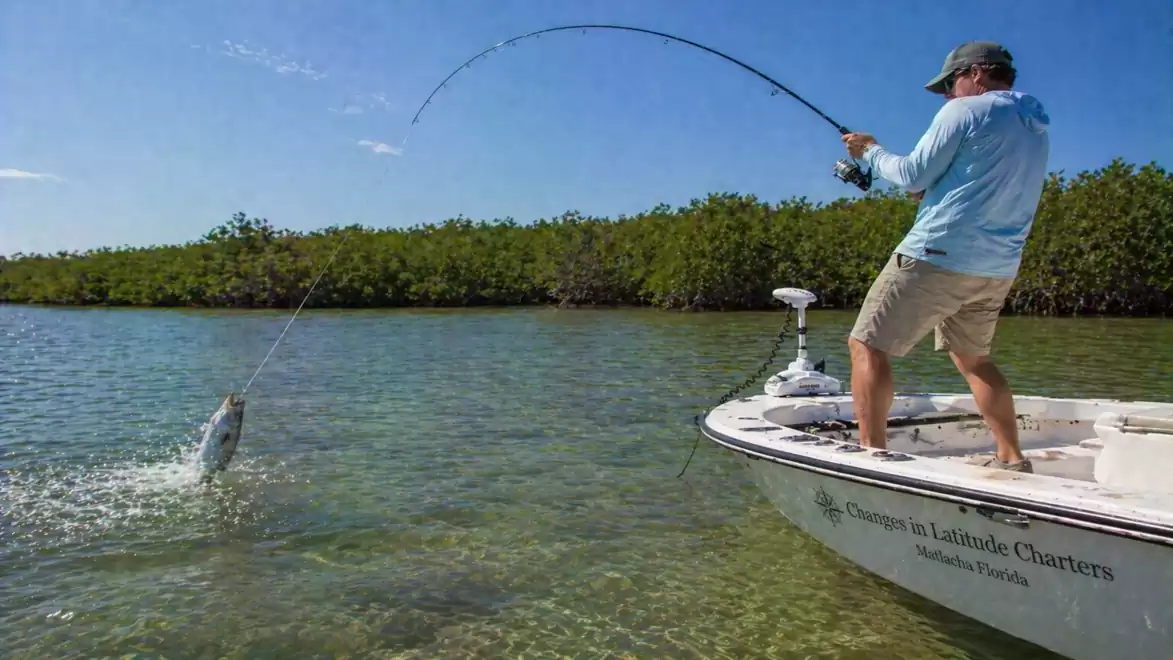 Man fishing on a boat, pulling a large fish out of the water.