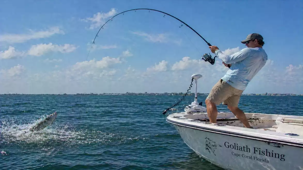 A man is fishing on a boat in the open sea with a large fish jumping out of the water.