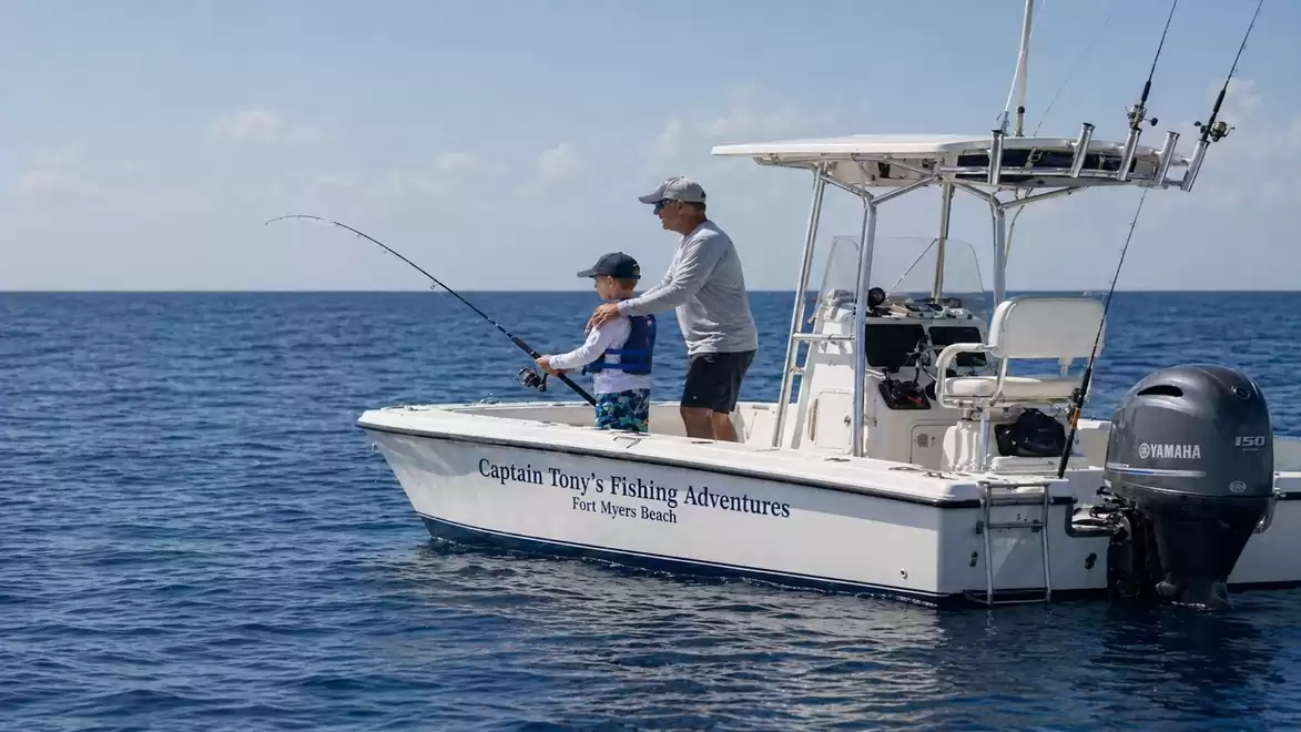 A small motorboat at sea with two people fishing. The boat has the inscription 'Captain Tony's Fishing Adventures'.