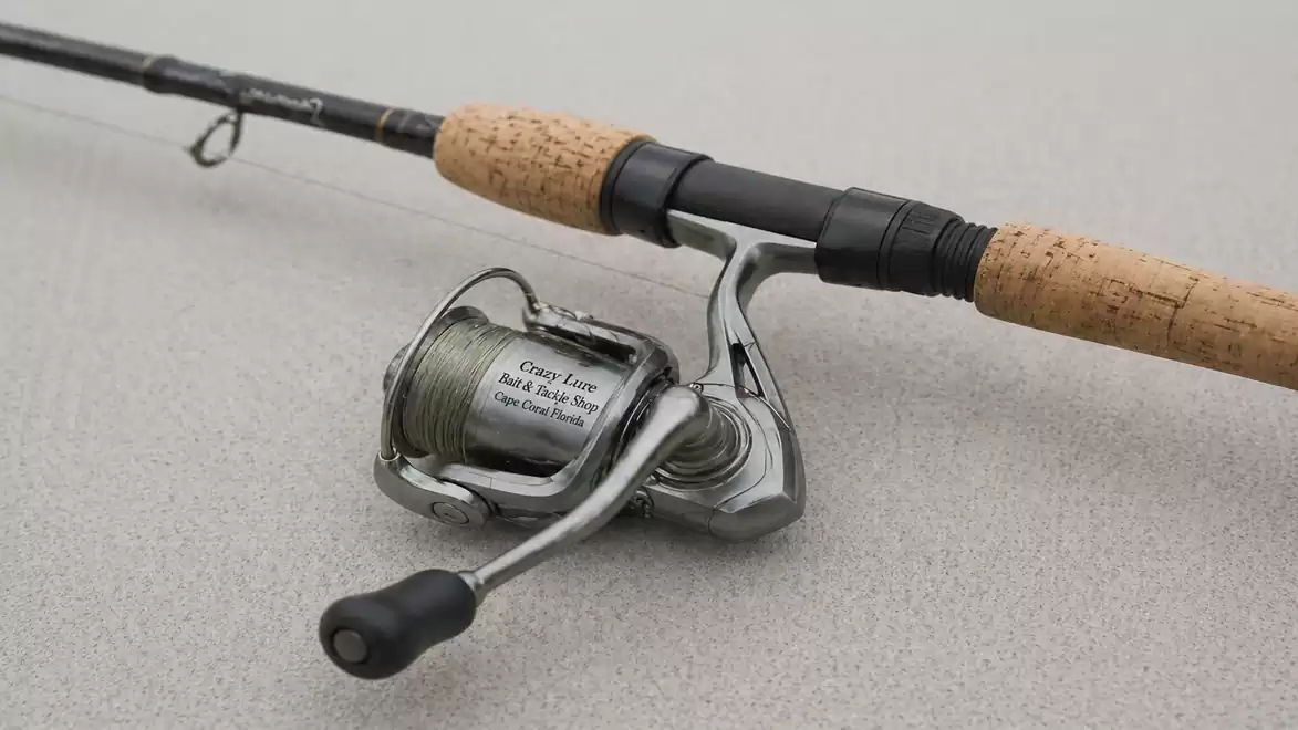 Close-up of a fishing rod with a cork handle and a silver reel on a light gray background.