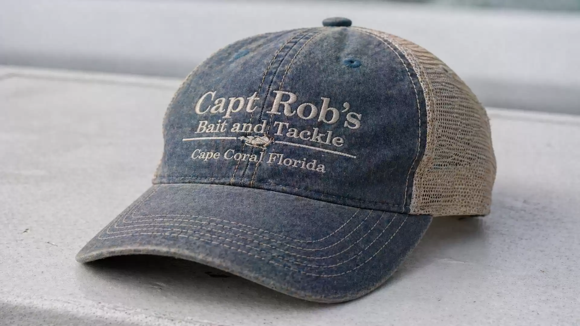 A dark blue baseball cap with the inscription 'Capt Rob's Bait and Tackle, Cape Coral Florida' on the front, lying on a surface.