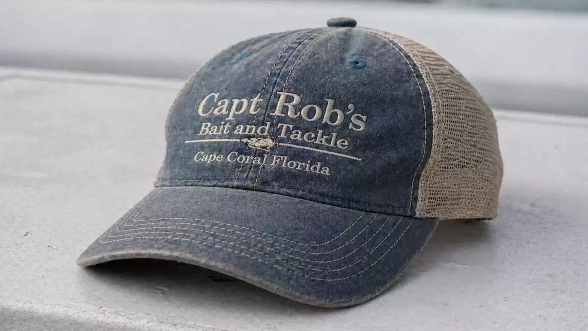 A dark blue baseball cap with the inscription 'Capt Rob's Bait and Tackle, Cape Coral Florida' on the front, lying on a surface.
