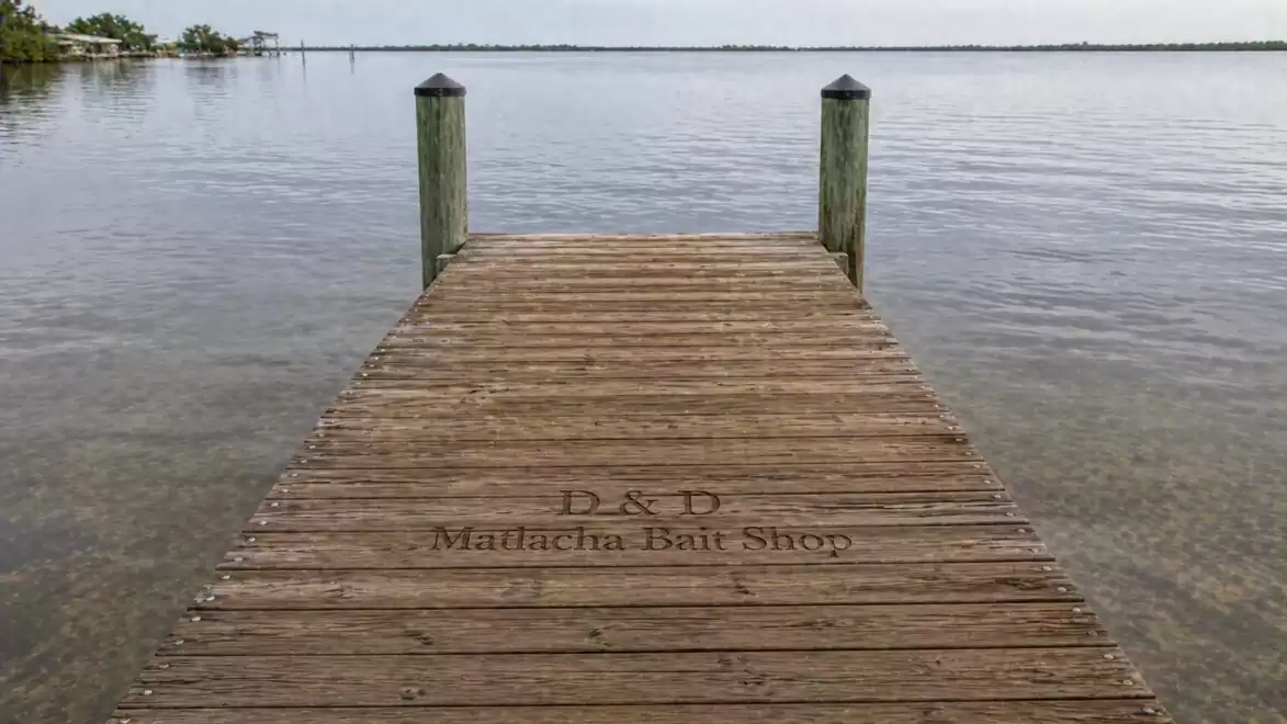 A wooden pier extends into a calm lake with two posts at its end. The sky is cloudy.