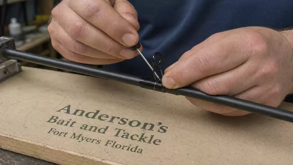 Close-up of hands repairing a fishing rod on a table labeled 'Anderson's Bait and Tackle, Fort Myers, Florida'.