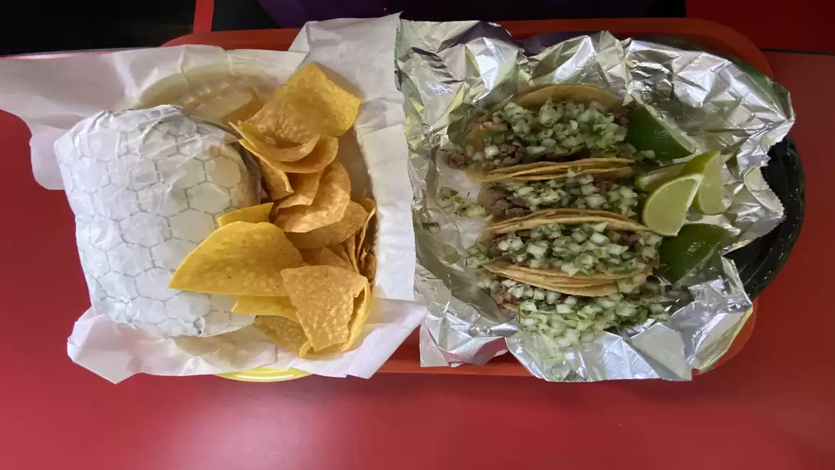 Burger with fries and tacos with limes on a red tabletop.