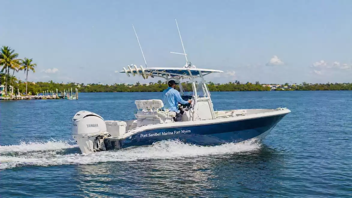 A modern motorboat speeds across the blue waters of a lake. A person in a blue shirt is steering under a clear, sunny sky.