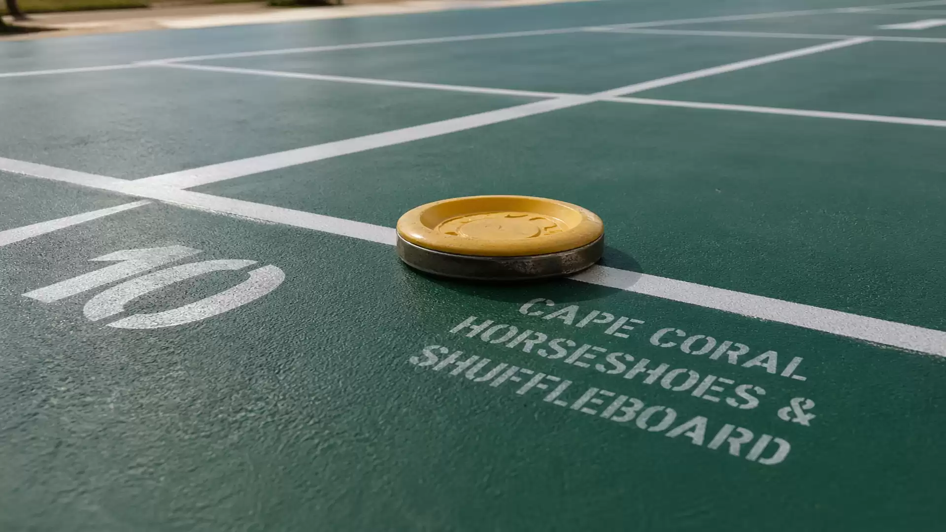 A close-up of a shuffleboard puck on a playing field at Cape Coral Horseshoes & Shuffleboard with the number 10 and markings on the ground.