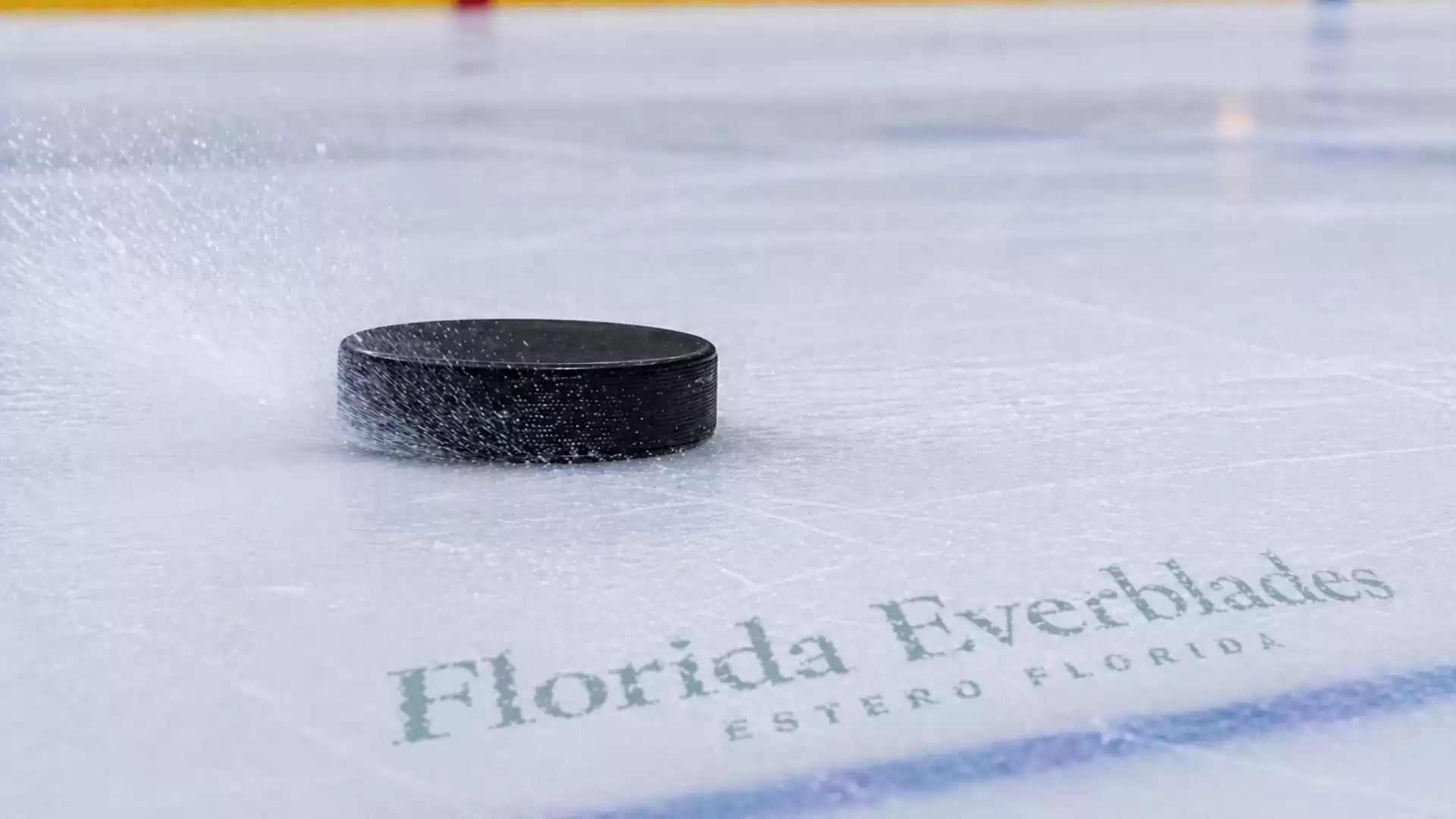 Close-up of a hockey puck gliding across the ice with the Florida Everblades logo in the background.