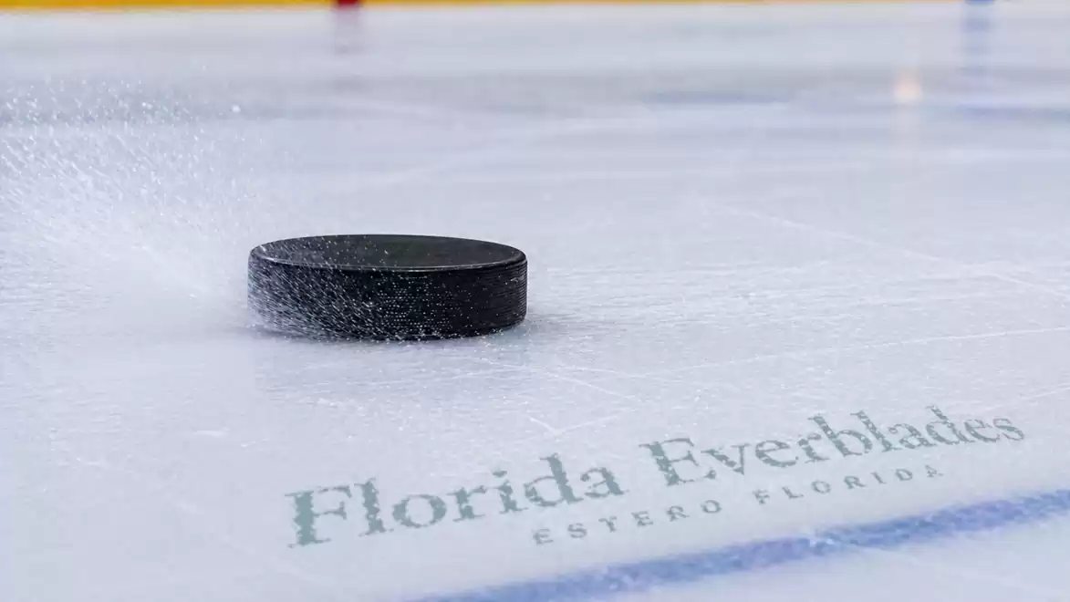Close-up of a hockey puck gliding across the ice with the Florida Everblades logo in the background.