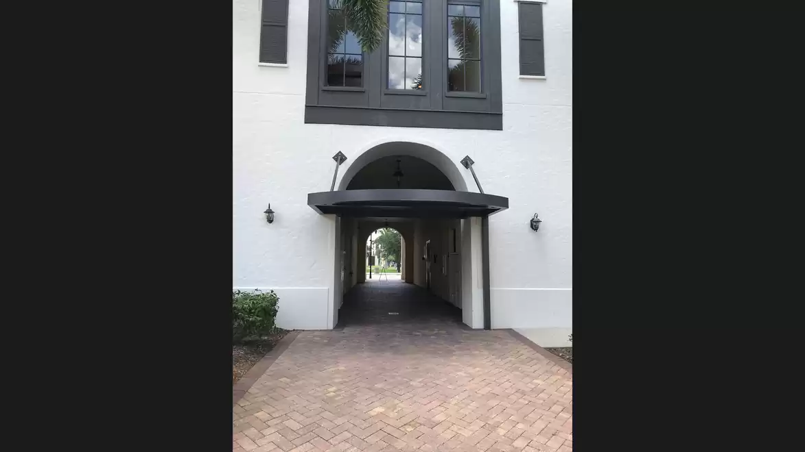 A building with an arched passageway and a paved floor. The building is white with dark window frames and two wall lamps on each side of the entrance.