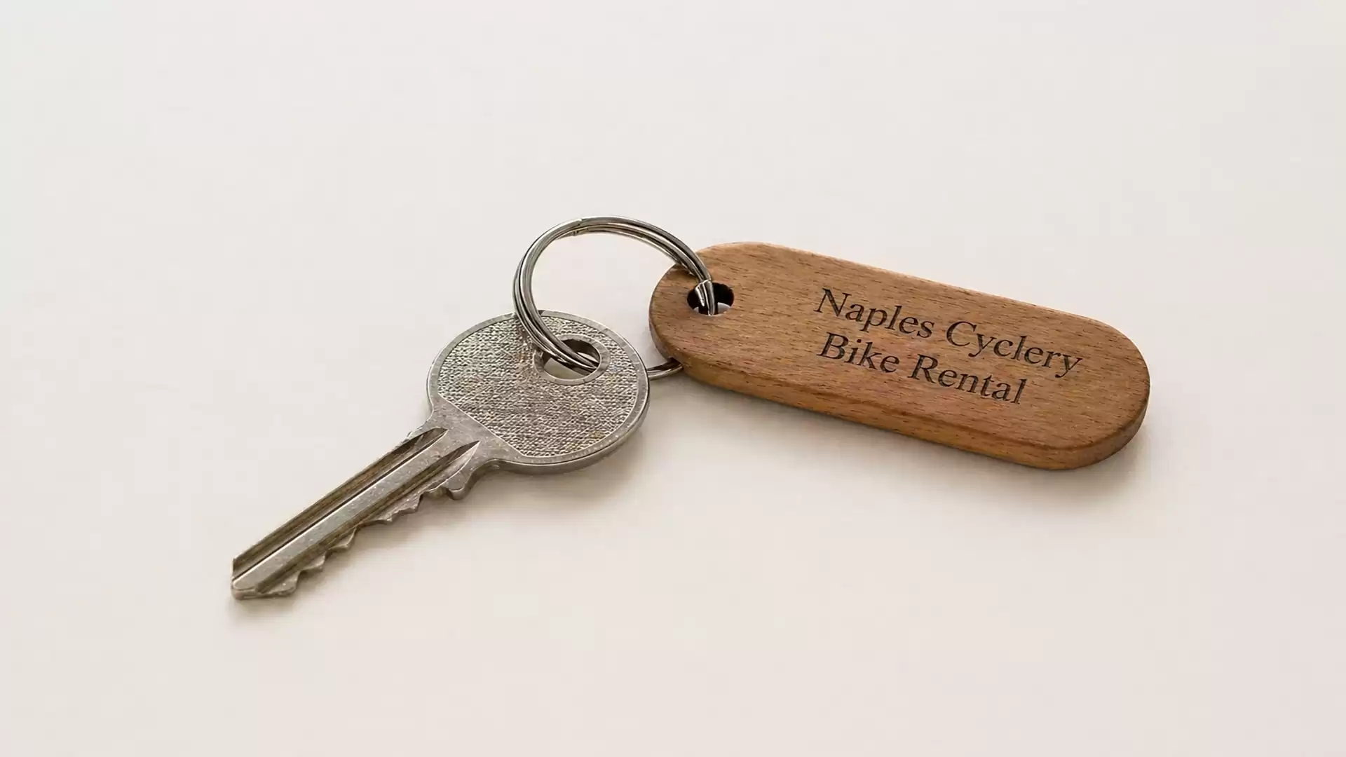 Close-up of a key with a wooden tag that reads 'Naples Cyclery Bike Rental' on a white background.