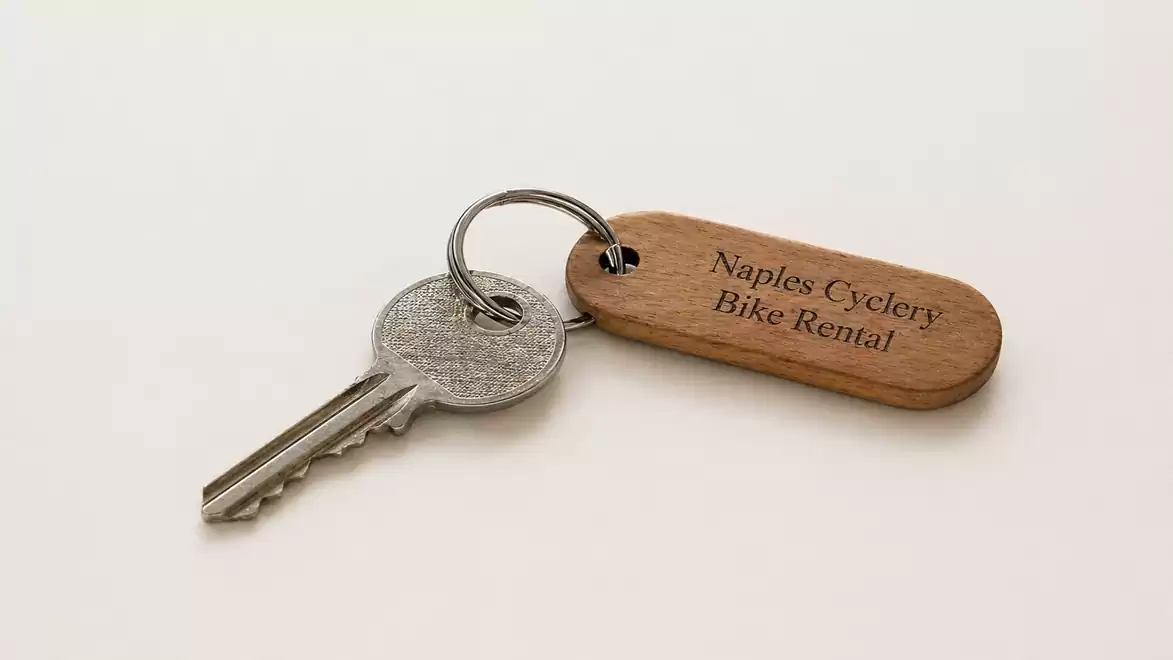 Close-up of a key with a wooden tag that reads 'Naples Cyclery Bike Rental' on a white background.