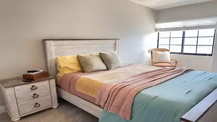 Cozy bedroom in wood look, colorful bedding, bedside table and armchair by the window. Bright and inviting