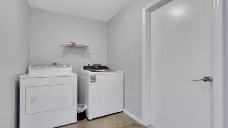Laundry room with white washer and dryer beside door and wall shelf