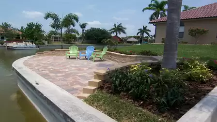 Paved canalfront terrace with colorful Adirondack chairs, low steps and landscaped flower beds