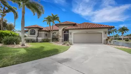 Single story house with red tile roof, driveway, lawn and canal on right