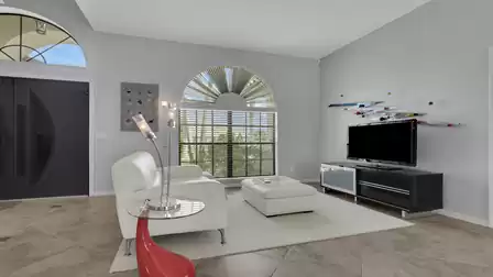 Living area with white armchairs, ottoman, TV stand and large arched window
