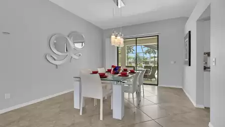Dining area with glass table, white chairs, wall art and sliding doors to patio