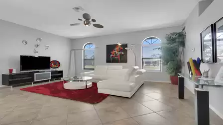 Living room with white sectional sofa, red rug, TV stand and arched windows