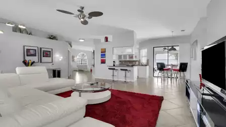 Open living area with white sectional, red rug, TV, breakfast bar and kitchen