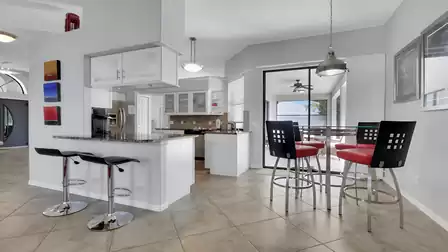 Kitchen with breakfast bar, red barstools, stainless appliances and sliding doors to lanai