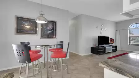 Open living area with round bar table, red stools, TV stand and wall clock