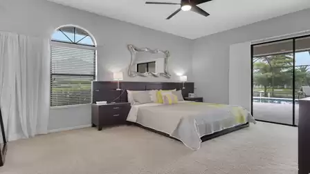Bedroom with double bed, dark wood furniture, arched window and sliding doors to pool