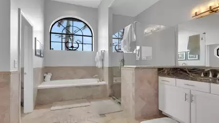 Bathroom with built-in tub, glass shower, granite vanity and arched window