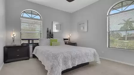 Bedroom with double bed, two dark nightstands, arched windows and patterned bedspread