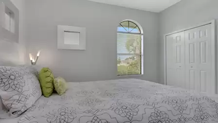 Bedroom with patterned bedspread, green accent pillows, arched window and double closet doors