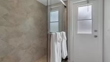 Tiled walk in shower with glass partition, white towels and frosted exterior door