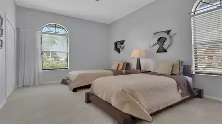 Bedroom with two single beds, arched windows, wall art and shared nightstand lamp