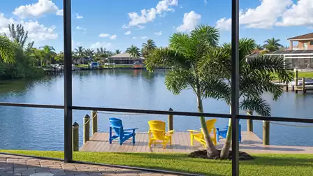 View through the screened lanai to the private dock on the canal with palm trees and seating