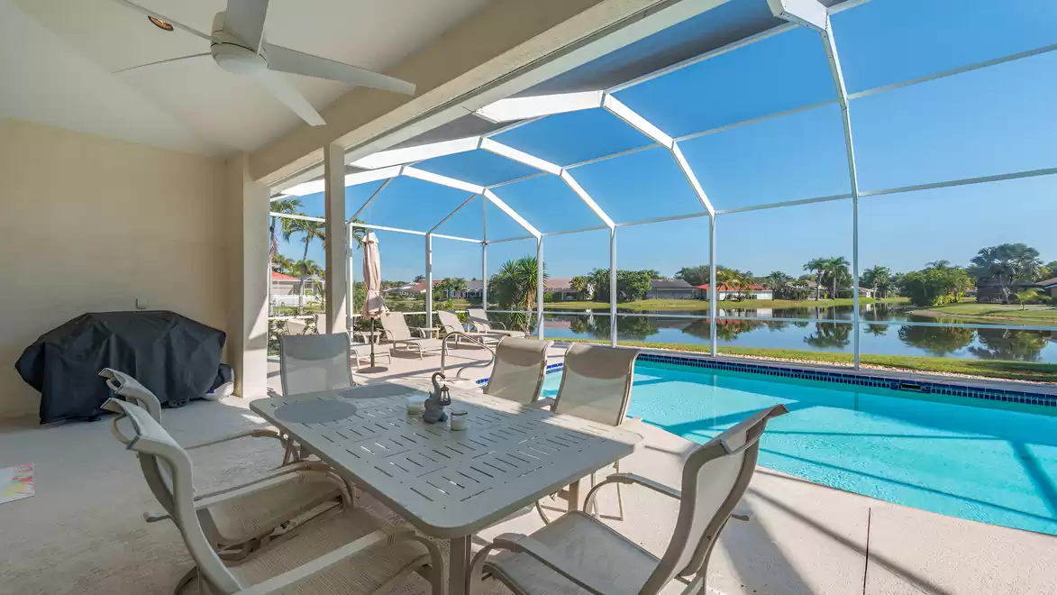 Covered pool terrace with dining table, sun loungers and private pool overlooking a tranquil lake and palm trees in Naples
