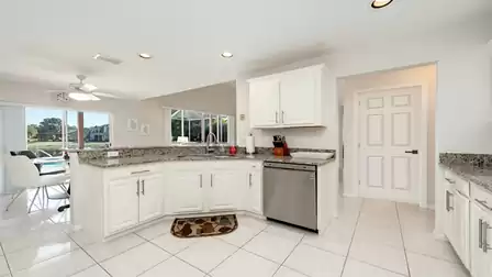 Modern, bright kitchen with white cabinets, granite countertops, dishwasher and view into the dining area.